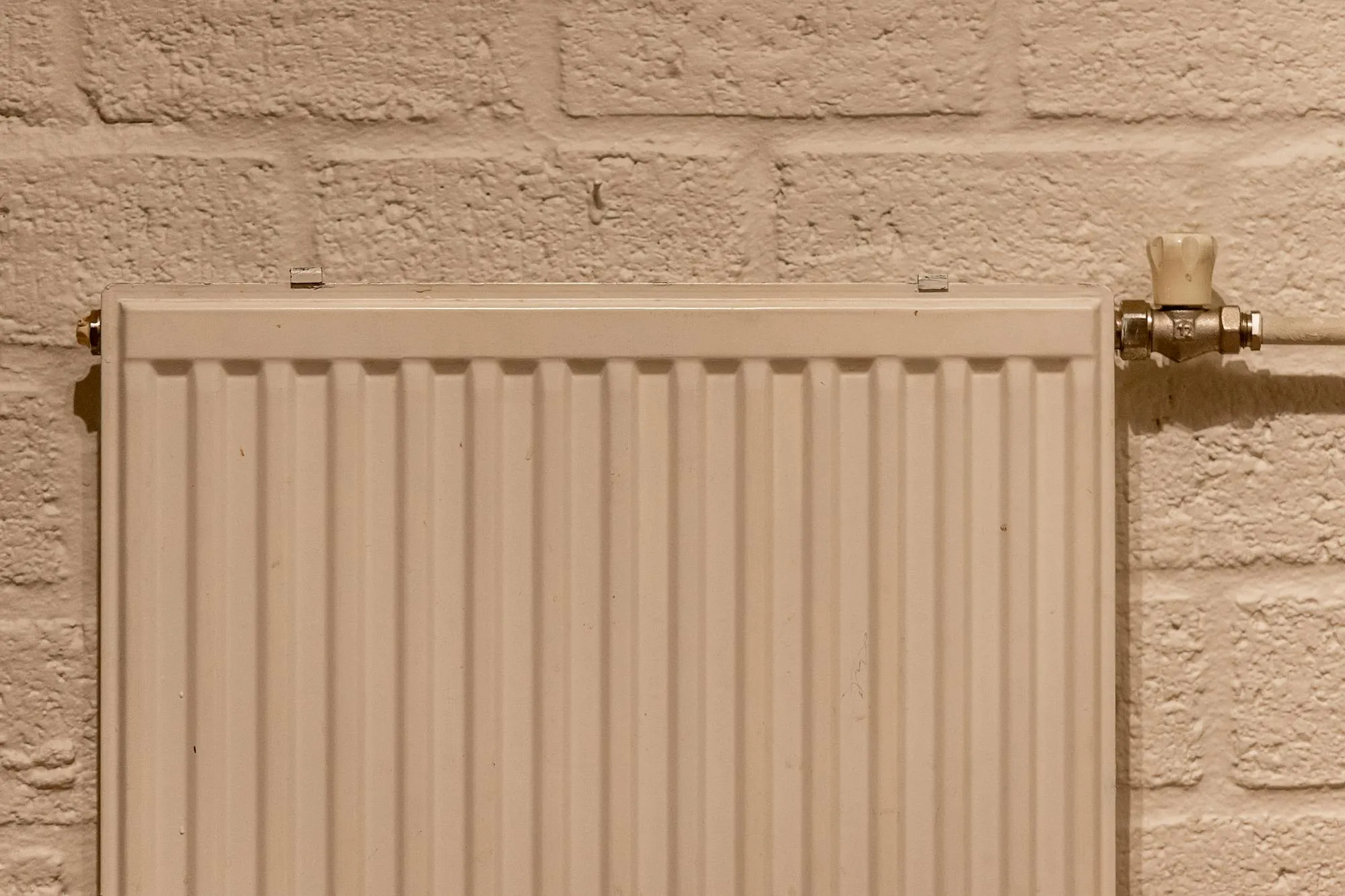 Modern UK panel radiator with a thermostatic valve, mounted on a painted brick wall.